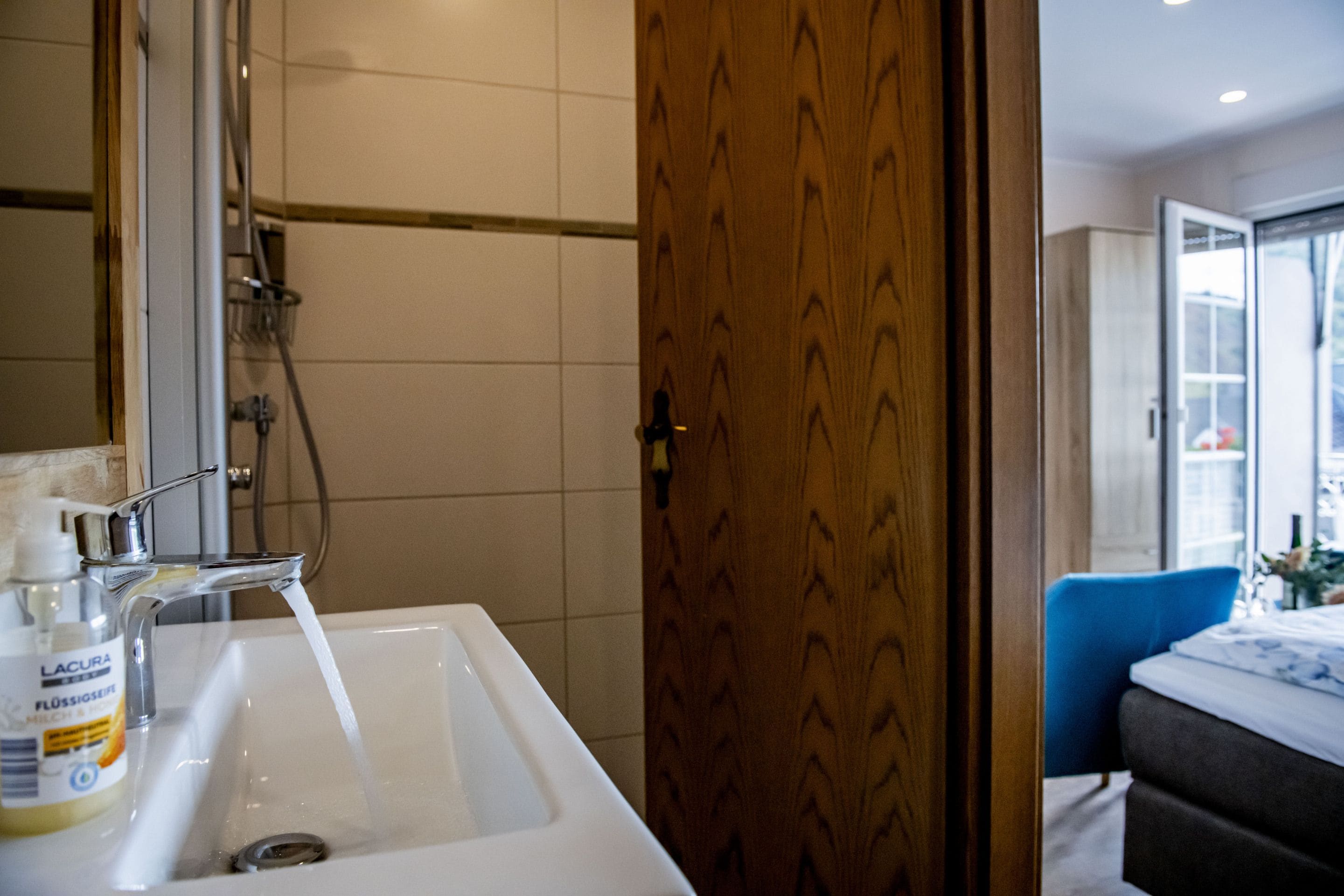 Ein Badezimmer mit einem weißen Waschbecken, einer Dusche und einer Holztür.