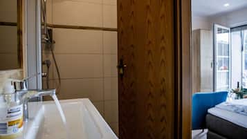Ein Badezimmer mit einem weißen Waschbecken, einer Dusche und einer Holztür.