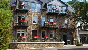 A multi-story stone building with balconies adorned with red flowers, a stone facade, and a sign reading "Landgasthof". - Das Gästehaus in Valwig (Valwig)
