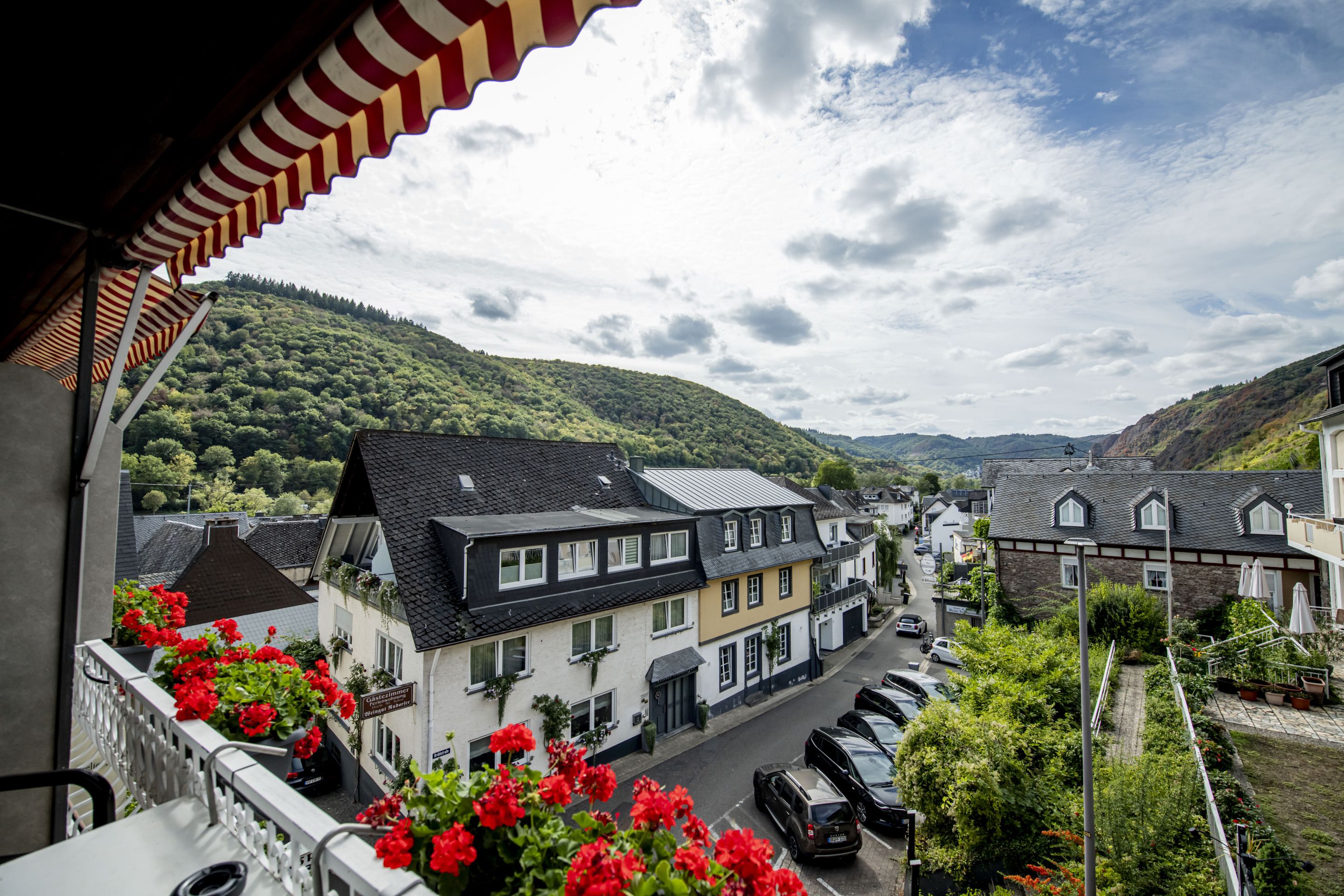 Eine Wohnstraße mit Häusern, parkenden Autos und einem Bergpanorama im Hintergrund.