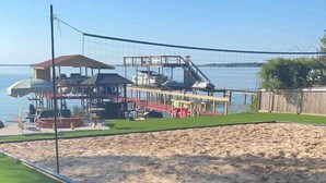 Een strandgebied met een volleybalnet, een overdekt zitgedeelte en een zandstrand.