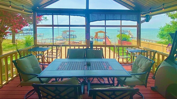 Een overdekt terras met een tafel en stoelen, met uitzicht op een strand en de oceaan.