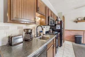 A kitchen with wooden cabinets, stainless steel appliances, a granite countertop, and a trash can.