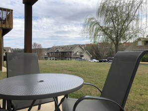 An outdoor seating area with a round table and chairs, a wooden deck, and a view of a residential building in the background.