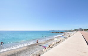 Ein Strand mit Kieselsteinen, blauem Himmel und wenigen Personen.