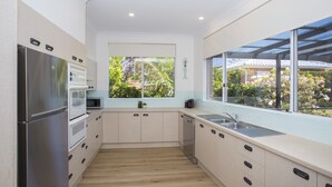 A modern kitchen with stainless steel appliances, light wood flooring, and large windows offering a view of greenery. - liandys@lakeconjola - close to lake, dog friendly (Lake Conjola)