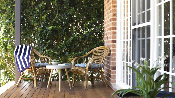 A wooden deck with wicker chairs and a table, surrounded by lush greenery. - liandys@lakeconjola - close to lake, dog friendly (Lake Conjola)