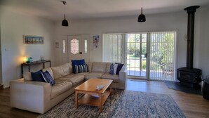 A living room with a beige sectional sofa, a wooden coffee table, and a patterned rug. There are two pendant lights, a fireplace, and a sliding glass door leading to a patio. - liandys@lakeconjola - close to lake, dog friendly (Lake Conjola)