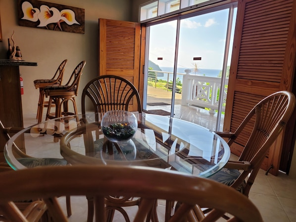 Enjoy meals at the glass-top dining table surrounded by wicker chairs, with a scenic view from the balcony through the glass door.
