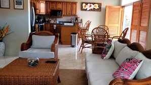 Amplia sala de estar con una cocina al fondo, muebles de mimbre y un comedor.