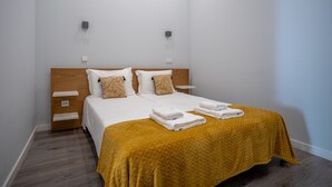 A neatly made bed with a yellow quilt, white pillows, and two bedside tables with lamps. - Foz do Douro - Apartment with garden (Oporto)