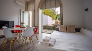 A modern hotel room with a large bed, a dining area with a table and chairs, a TV, and a view through an open archway to an outdoor area. - Foz do Douro - Apartment with garden (Oporto)