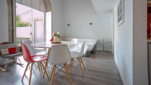A modern dining area with a round table, white chairs, and a bench with cushions. - Foz do Douro - Apartment with garden (Oporto)