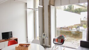 A modern room with a large window, a round table, a television, and a box labeled "MONTES ERMOS". - Foz do Douro - Apartment with garden (Oporto)