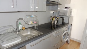 A modern kitchen with grey cabinets, a stainless steel sink, a built-in washing machine, and a countertop with various kitchen items.
