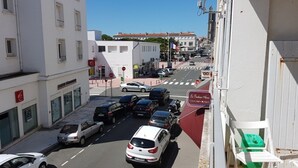 A street view with parked cars, a pedestrian crossing, and buildings with signage.
