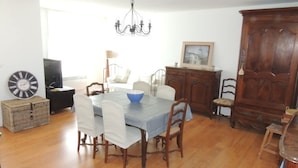 A dining area with a table, chairs, a chandelier, a wooden cabinet, and a television.