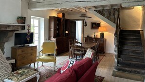 A rustic room with exposed wooden beams, a dining table with chairs, a red sofa, a television, and a staircase. - 18th C House, Own Pool, Mountain, River Views, peaceful and private. (Pyrenees Atlantiques, Pays Basque)