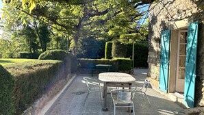 A garden patio with a round table and chairs, surrounded by stone walls and greenery. - 18th C House, Own Pool, Mountain, River Views, peaceful and private. (Pyrenees Atlantiques, Pays Basque)