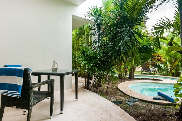 A patio area with a table and chairs, a small pool, and lush tropical plants.