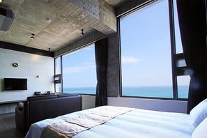 A modern hotel room with a large bed, a flat-screen TV, a desk, and a view of the ocean. - Guesthouse Ocean View (Shoufeng)
