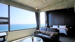 Een moderne hotelkamer met een groot raam met uitzicht op zee, een bank, een bed en een kleine tafel met een plant.