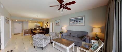 A spacious living room with a grey sofa, patterned armchairs, a wooden coffee table, and a ceiling fan.
