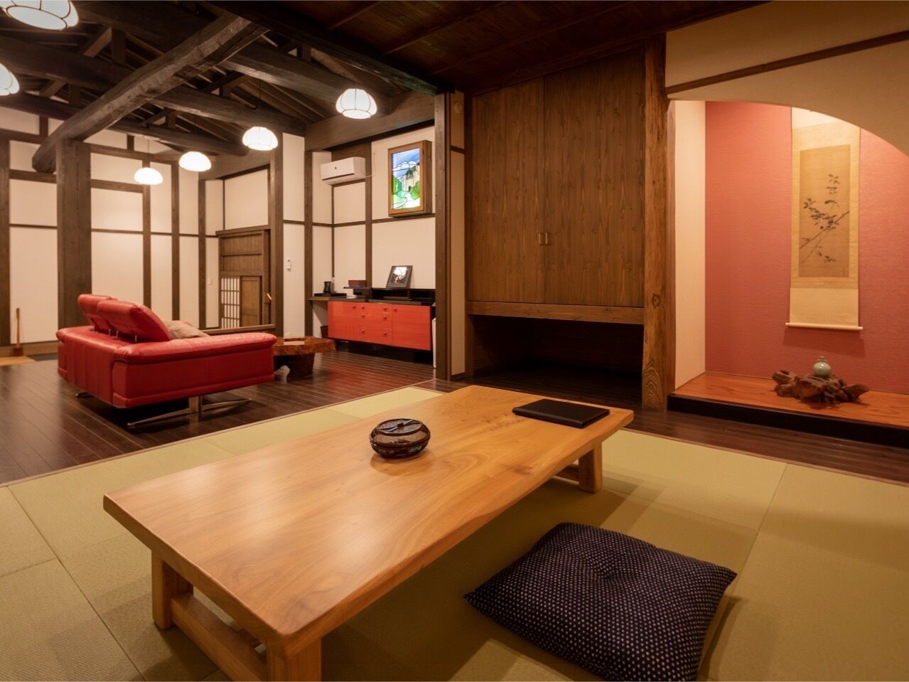 Una tradizionale stanza giapponese con pavimento in tatami, un tavolino in legno, un divano rosso e una porta scorrevole che dà su un'altra stanza.