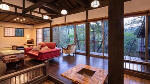 A traditional Japanese-style room with tatami flooring, a red sofa, a wooden table, and large windows offering a view of the forest. - Hanarenoyado Sennomori (Aso)