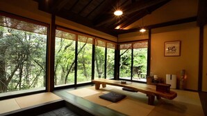 A traditional Japanese room with tatami flooring, a wooden bench, and large windows offering a view of lush greenery. - Hanarenoyado Sennomori (Aso)