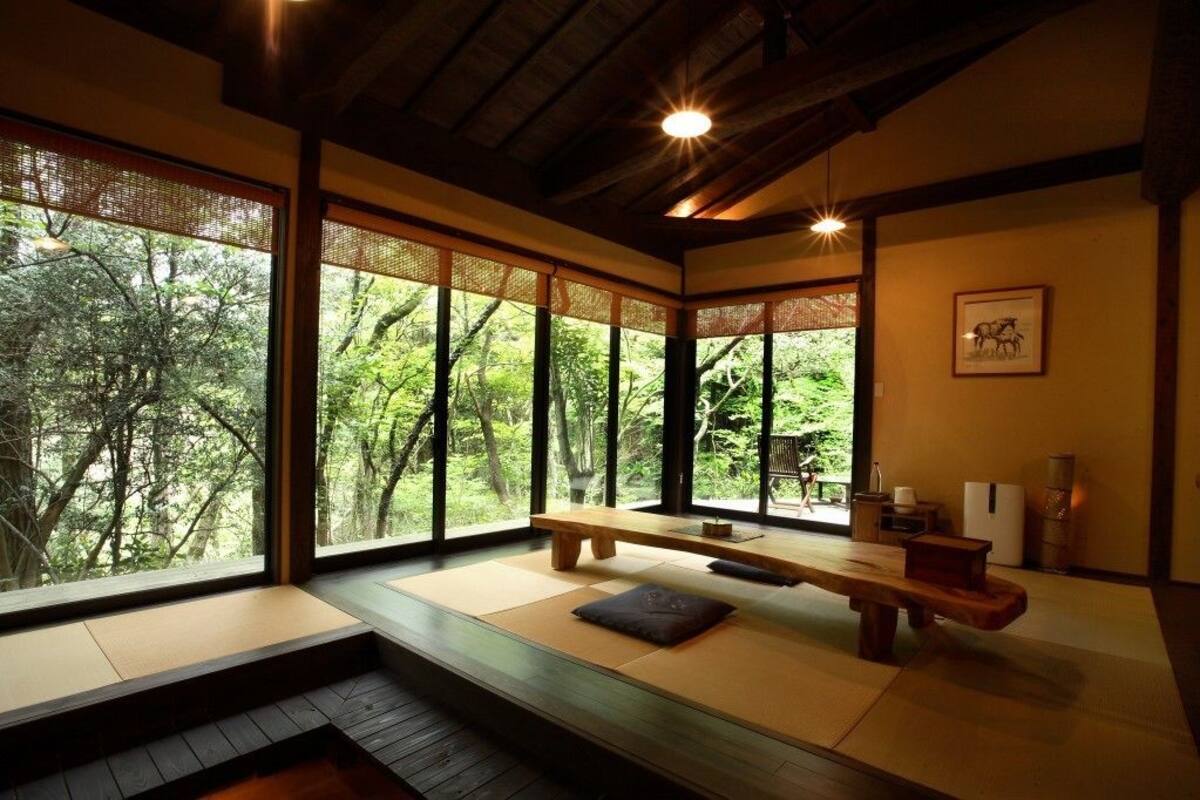 Ein traditioneller japanischer Raum mit Tatami-Bodenbelag, einer Holzbank und großen Fenstern mit Blick auf üppiges Grün.