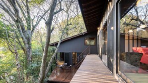 A modern house with a wooden deck, large windows, and a view of the surrounding forest. - Hanarenoyado Sennomori (Aso)