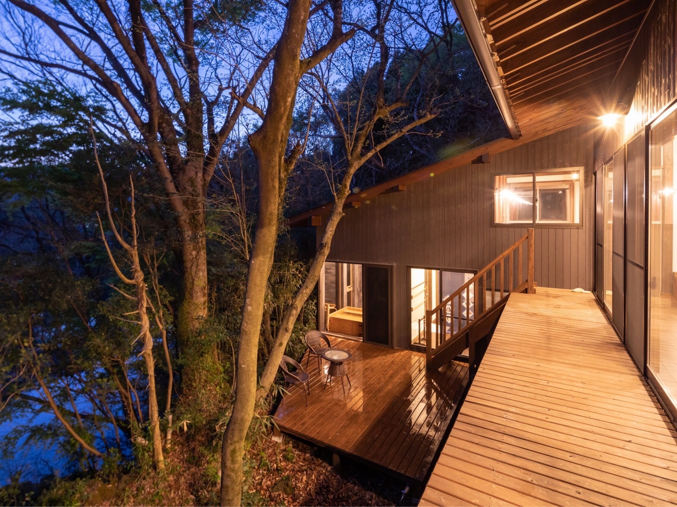 A wooden deck with a table and chairs, overlooking a body of water and surrounded by trees.