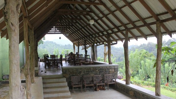 An outdoor covered patio with stone steps leading to a seating area with wooden chairs and tables, overlooking a lush green landscape.