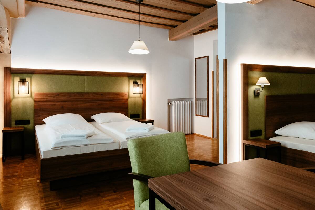 Une chambre d’hôtel avec deux lits, une table en bois, une chaise verte et un plafond en bois.