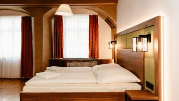 A bedroom with a wooden bed, a nightstand, a wall-mounted lamp, and a window with curtains.