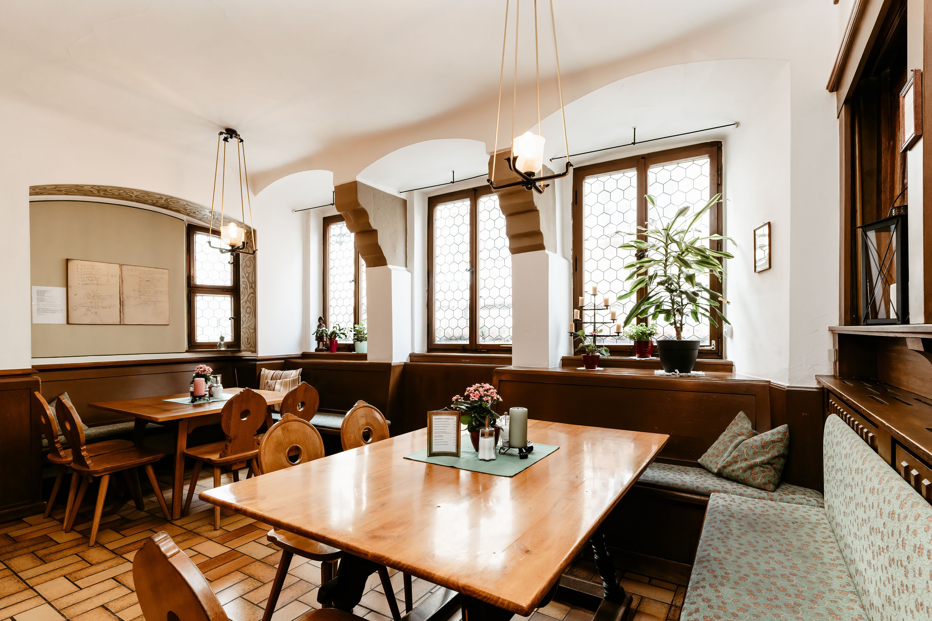 A cozy dining area with wooden furniture, a large table, and a bench. There are potted plants and a hanging light fixture.
