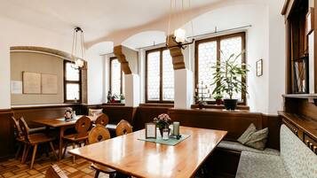 A cozy dining area with wooden furniture, a large table, and a bench. There are potted plants and a hanging light fixture.
