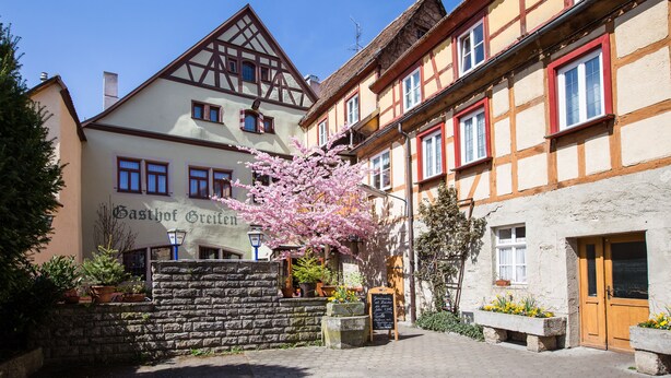 A traditional European building with a stone wall, a wooden door, and a sign that reads "Gasthof Greifen". - Hotel-Gasthof Goldener Greifen (Rothenburg ob der Tauber)