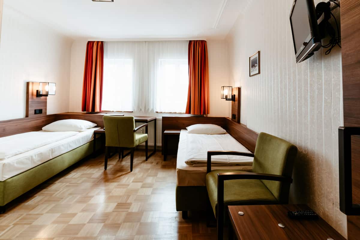 Une chambre d’hôtel avec deux lits simples, un bureau, une chaise et un téléviseur fixé au mur.