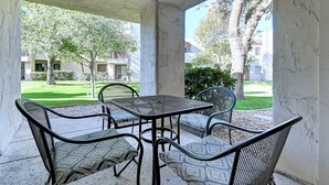 Ein überdachter Außenbereich mit Tisch und Stühlen, der auf eine gepflegte Rasenfläche und Gebäude im Hintergrund blickt.