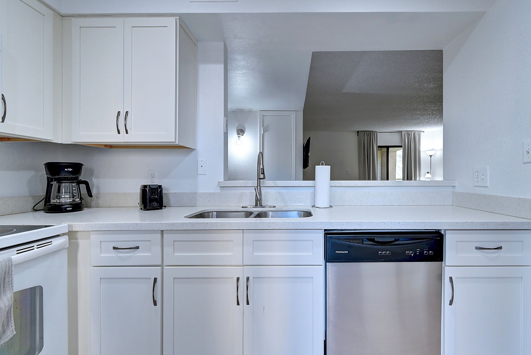 A modern kitchen with white cabinets, a stainless steel sink, a coffee maker, and a dishwasher.