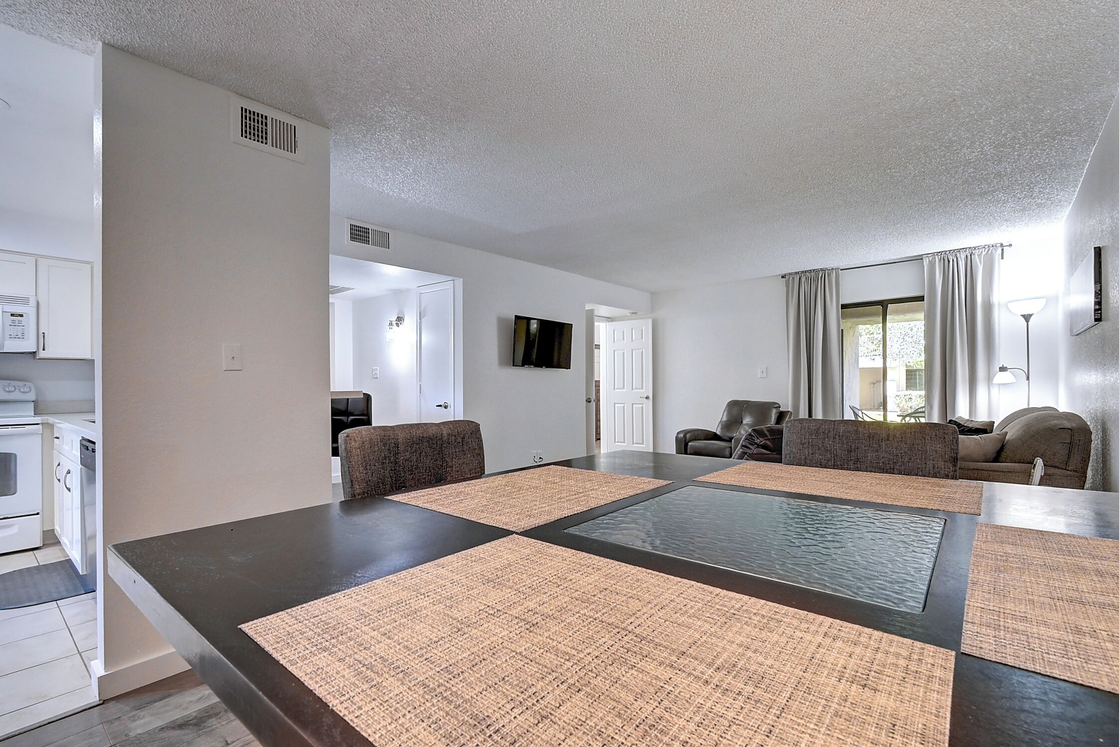 A modern living room with a dark floor, a large central table, and a kitchen area with white cabinets and appliances.