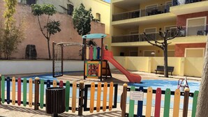 Area giochi per bambini con scivolo e struttura di arrampicata, delimitata da una recinzione colorata.
