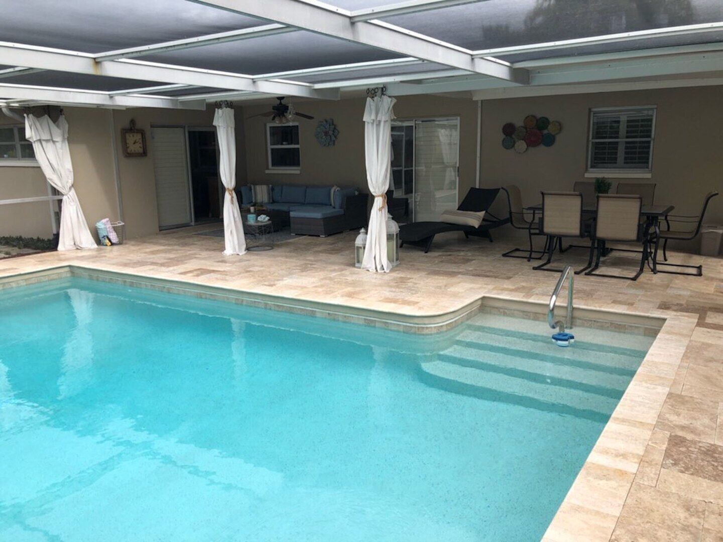 A swimming pool with a sunken seating area, a covered patio, and a dining area with outdoor furniture.
