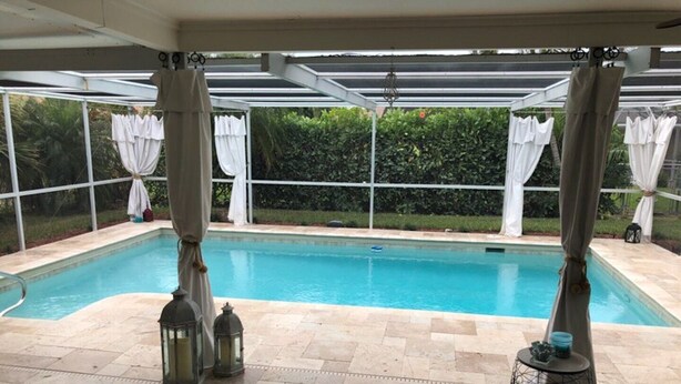 Ein überdachter Außenpool mit einer Pergola, Steinböden und einer Liege.