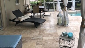 Ein überdachter Patio-Bereich mit Pool, Gartenmöbeln und Deckenventilator.