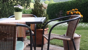 A patio area with wicker furniture, a table with a striped tablecloth, and potted plants. - Landhaus Seehof (Fuessen)