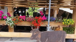 A rustic outdoor setting with a wooden structure, a metal cow sculpture, and colorful flower arrangements. - Landhaus Seehof (Fuessen)