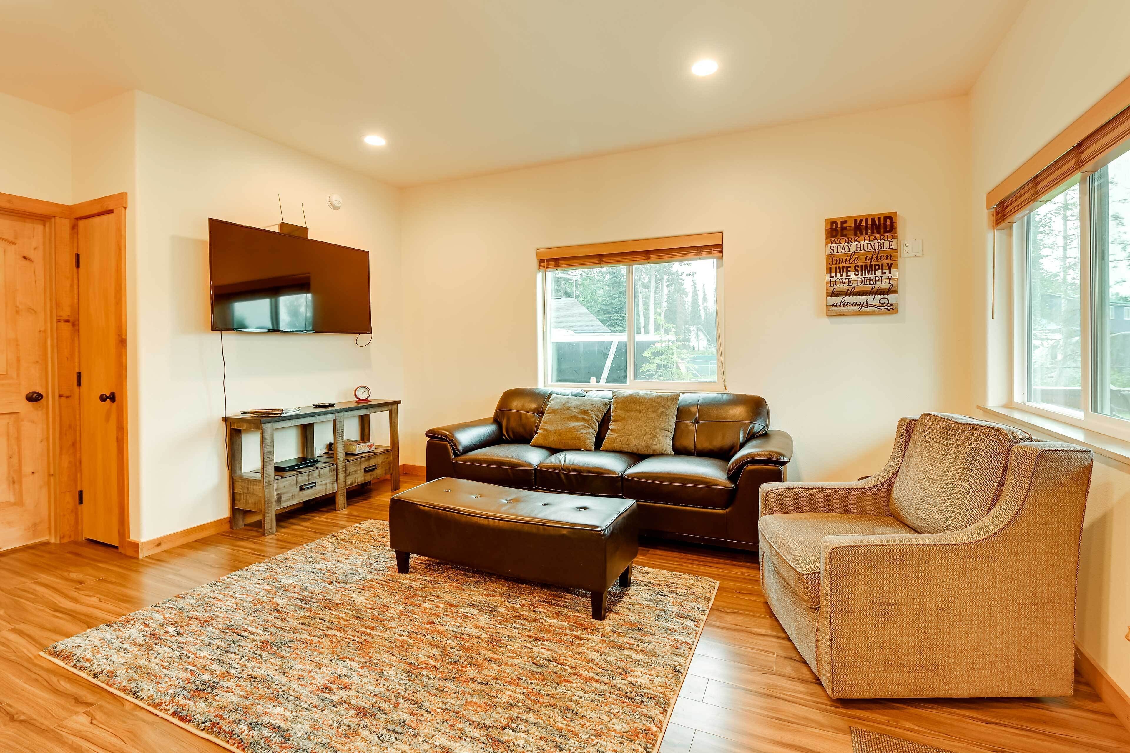 A living room with a leather sofa, a brown armchair, a wooden coffee table, and a large window with blinds.